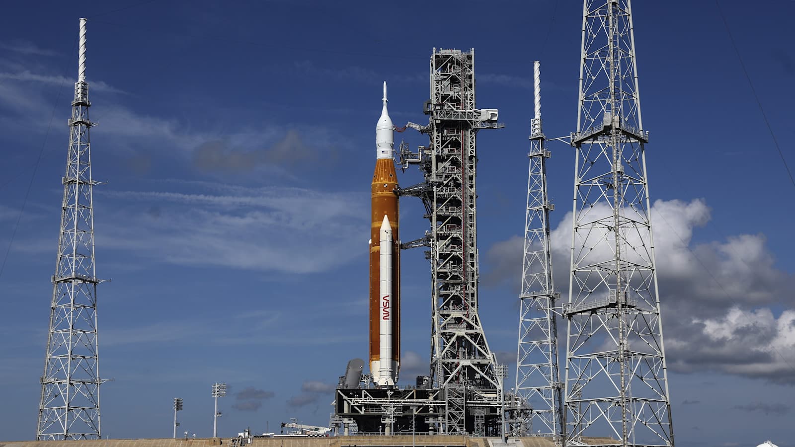 rocket against blue sky partly cloudy with metal antennae in the foreground. 