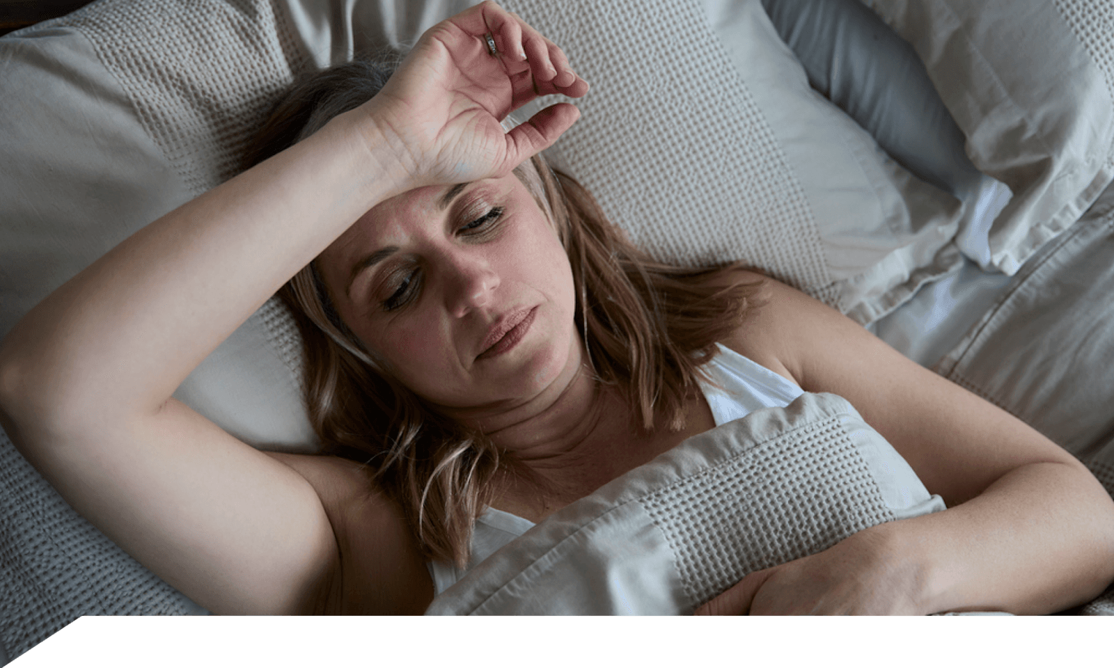 Woman laying on her back in bed with forearm across forehead