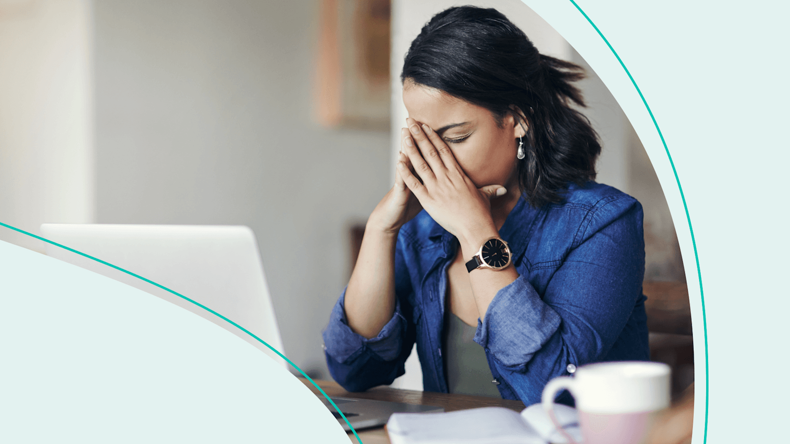 Person with shoulder-length black hair sitting in front of a laptop with their hands on their face