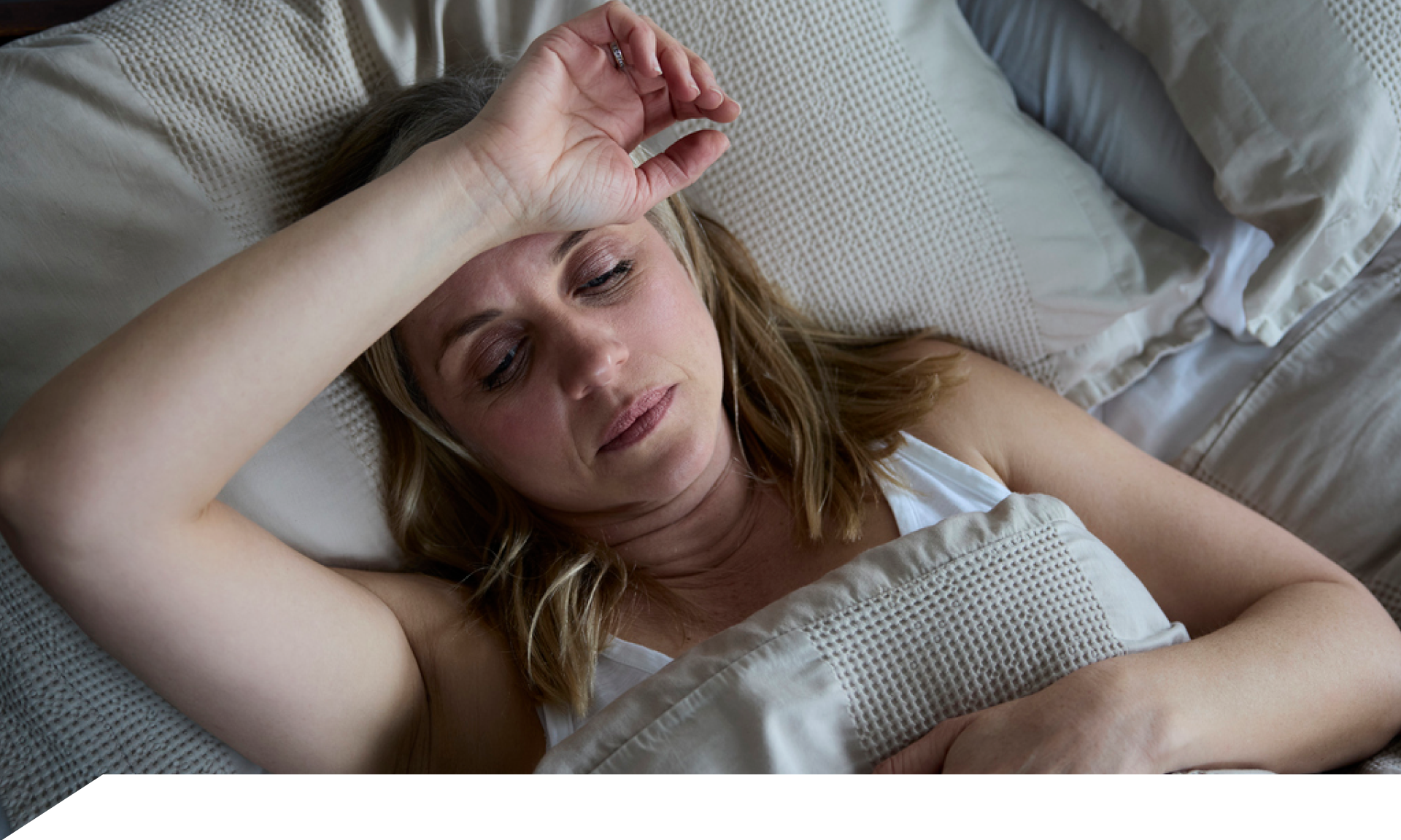 Woman laying on her back in bed with forearm across forehead