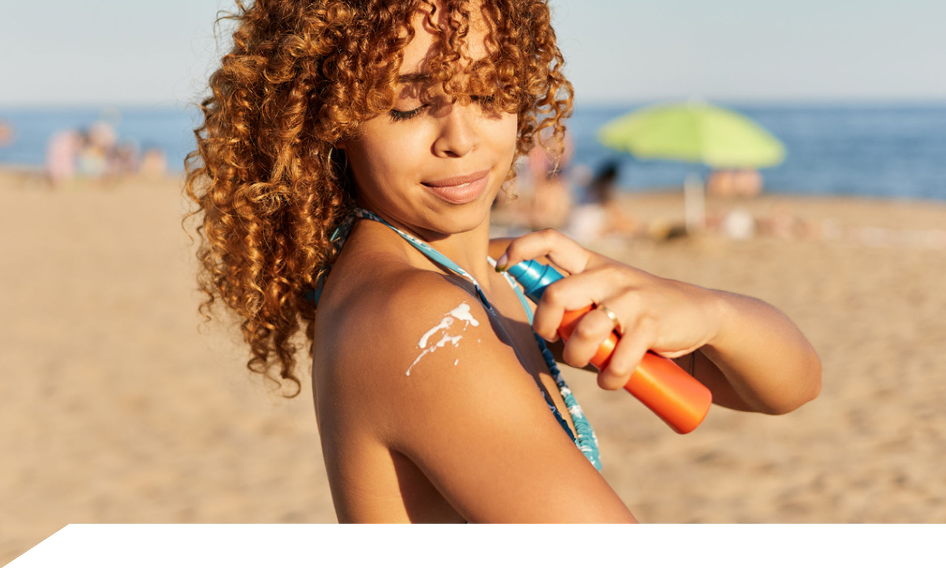 A woman applying sunscreen to her shoulder at a beach