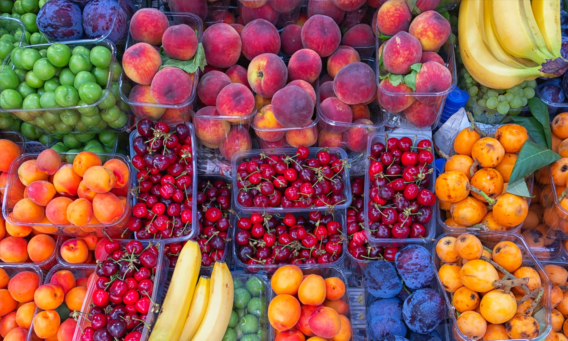 peaches, cheeries, bananas, and other fruit side by side at a market