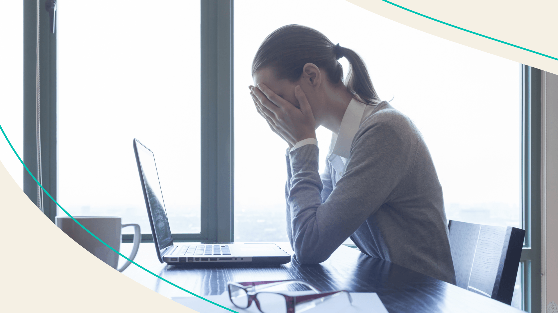 A woman sitting in front of her laptop at work with her face in her hands