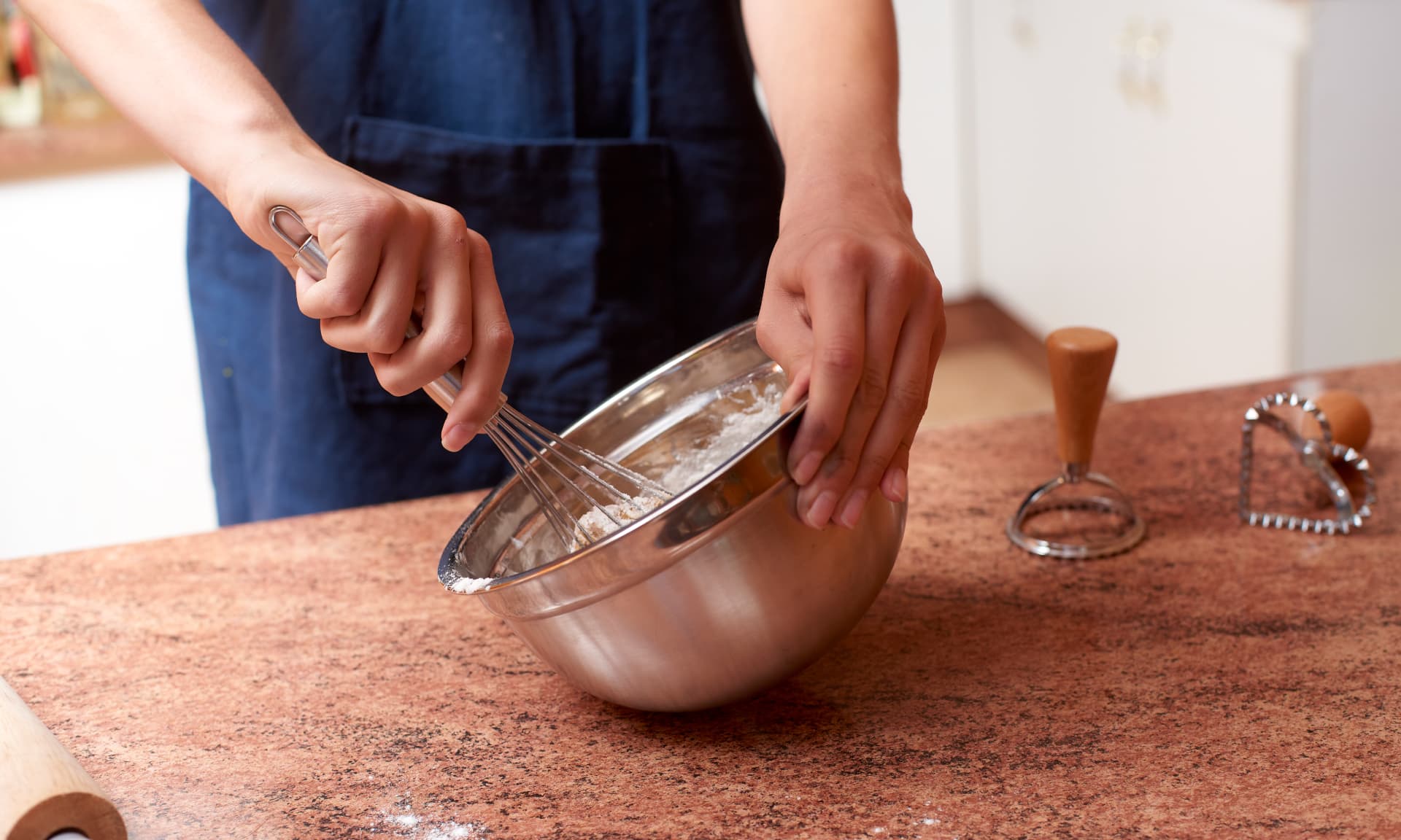 Person wearing blue apron mixing baking ingredients in a bowl with a whisk
