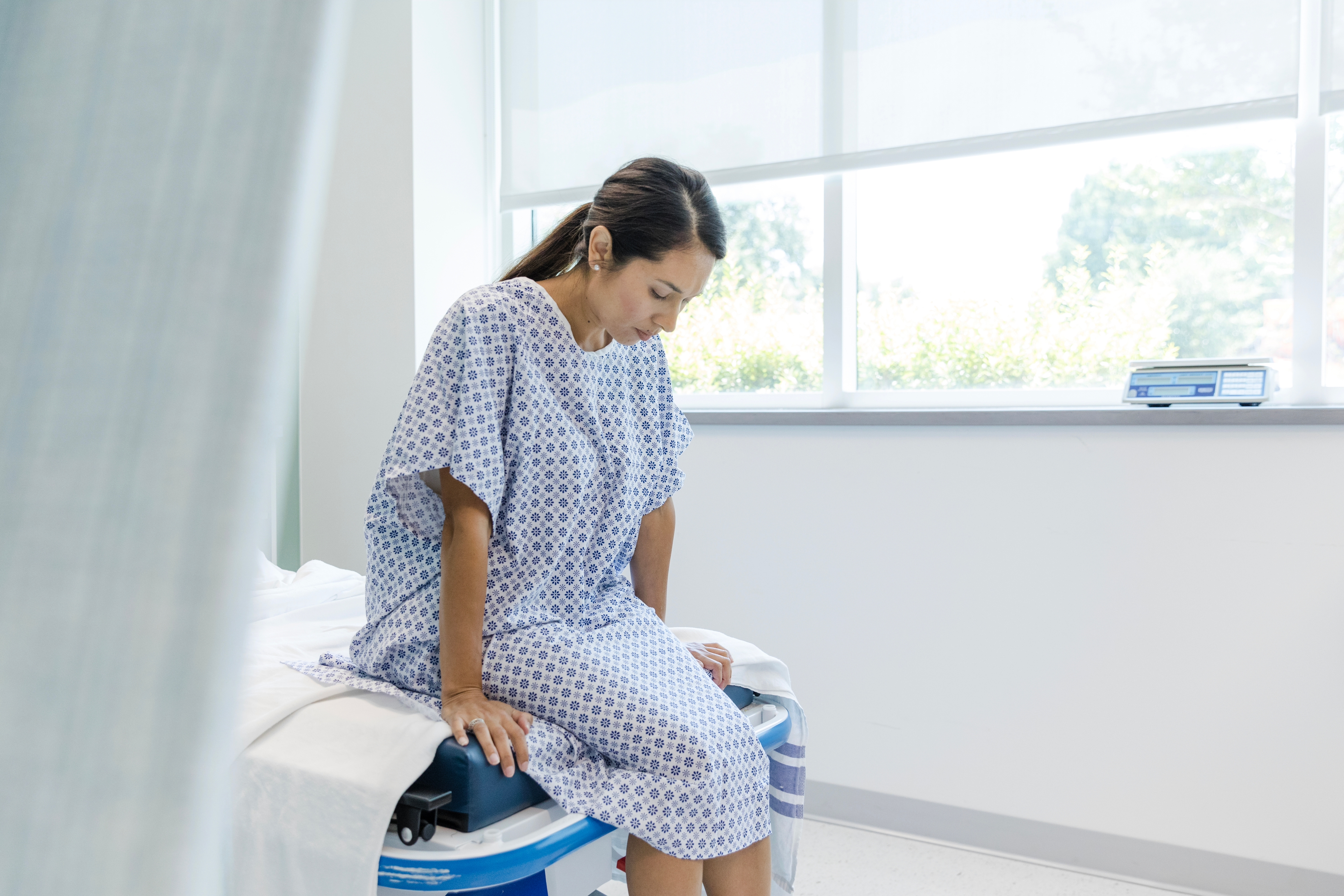 Looking down, woman in hospital gown waits for test results