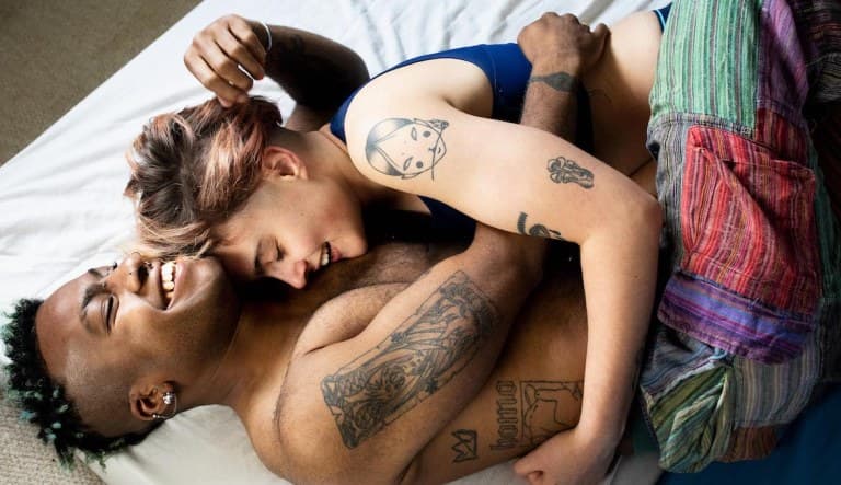 A young couple laughs and hugs one another in bed. This photo is being used to promote an article about sex personality types.