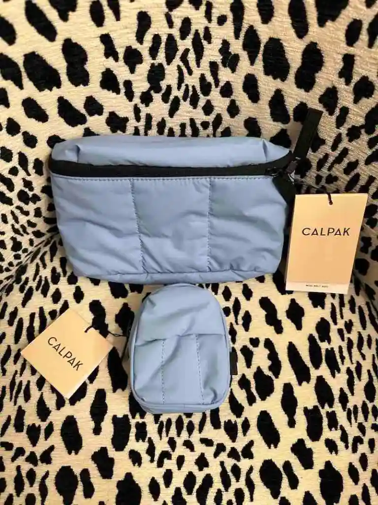 Blue Calpak belt bag and backpack charm on cheetah print chair
