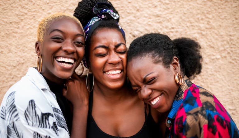 Three women smiling with their eyes closed; how to be happy single