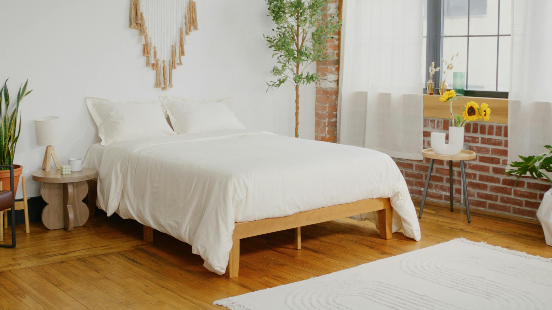 A bedroom with wooden floors and a large bed with all white bedding on a wooden frame.